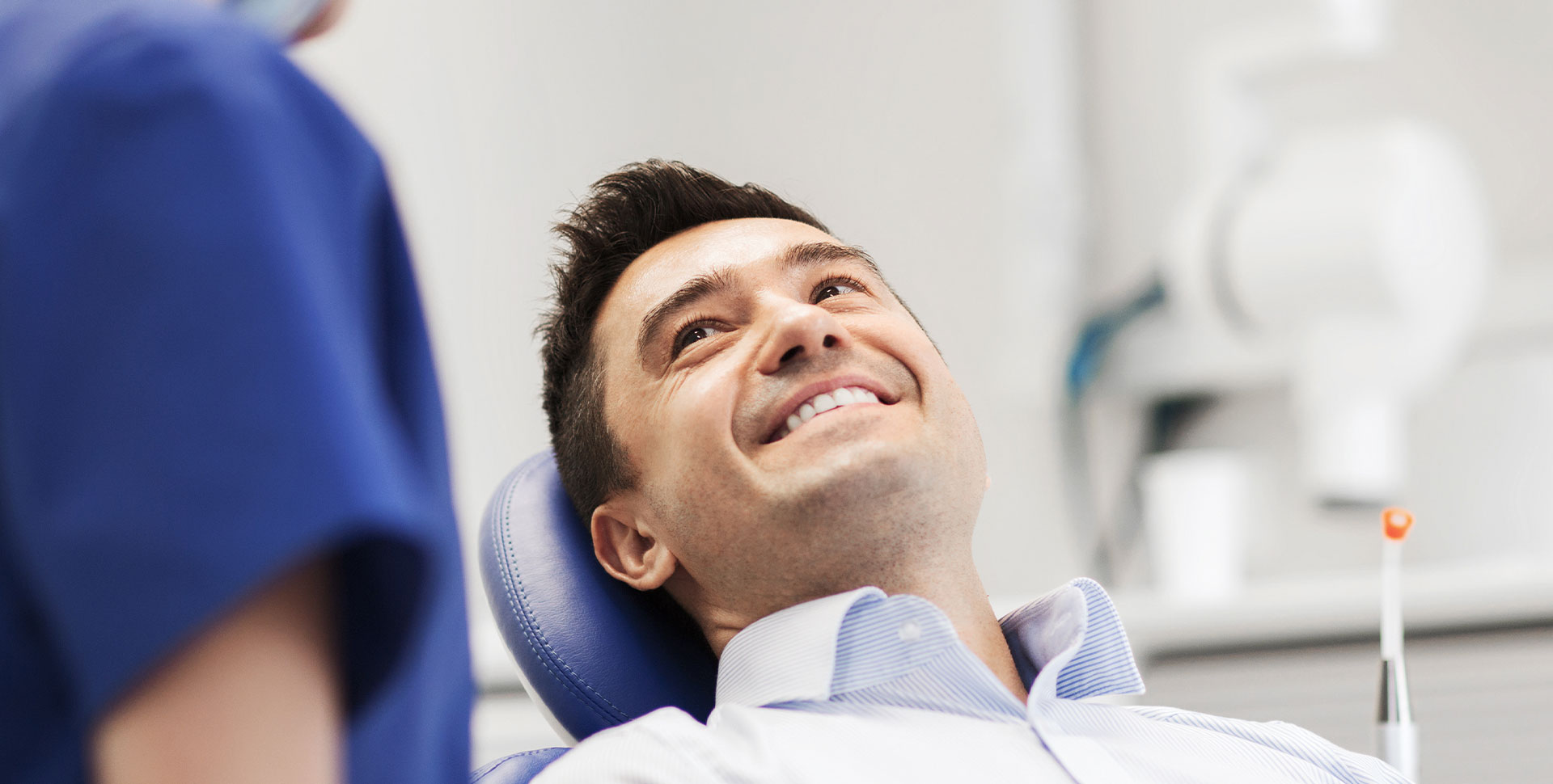 A smiling man in a dental chair being attended to by a dentist.