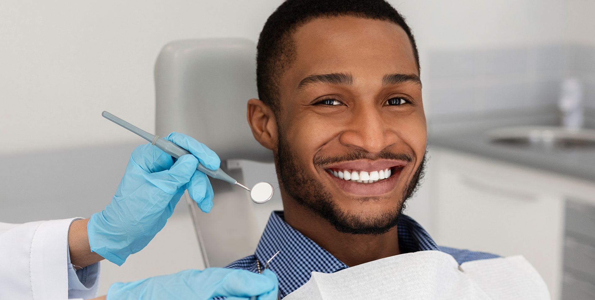 A smiling man receiving dental treatment, with a dental hygienist in the background.