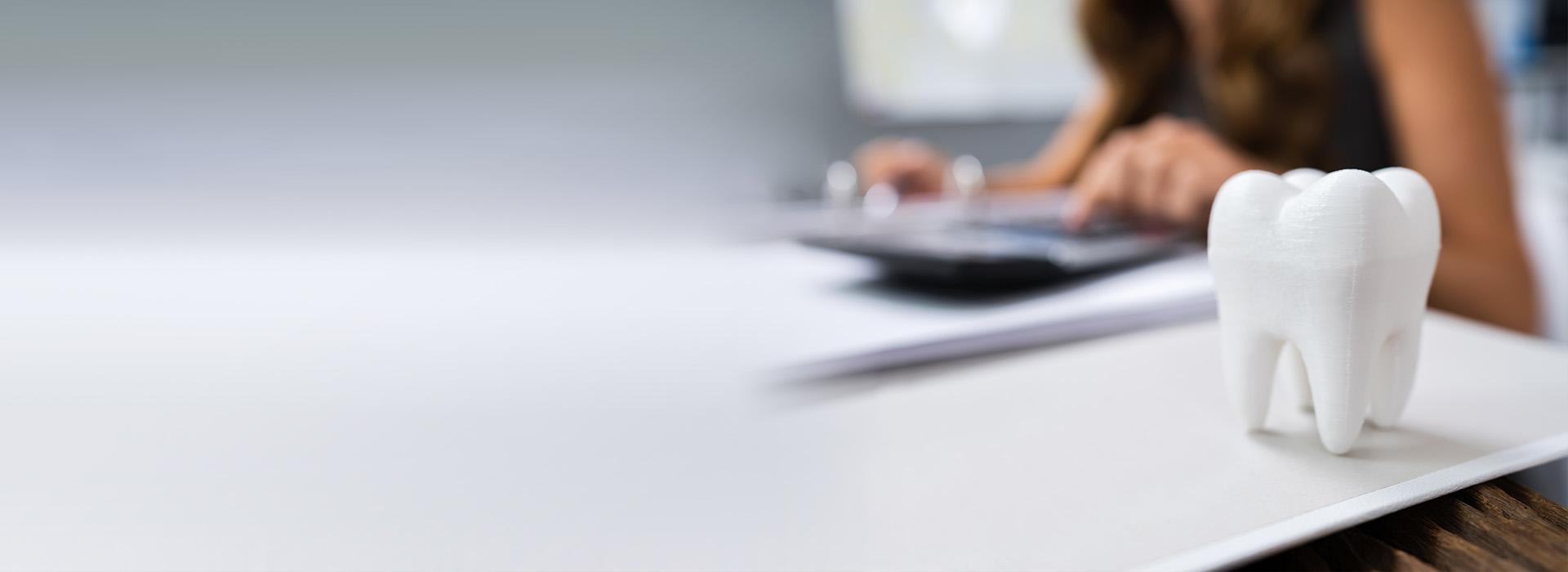 The image shows a person sitting at a desk with a laptop and papers, wearing a white mask that resembles a smiley face.