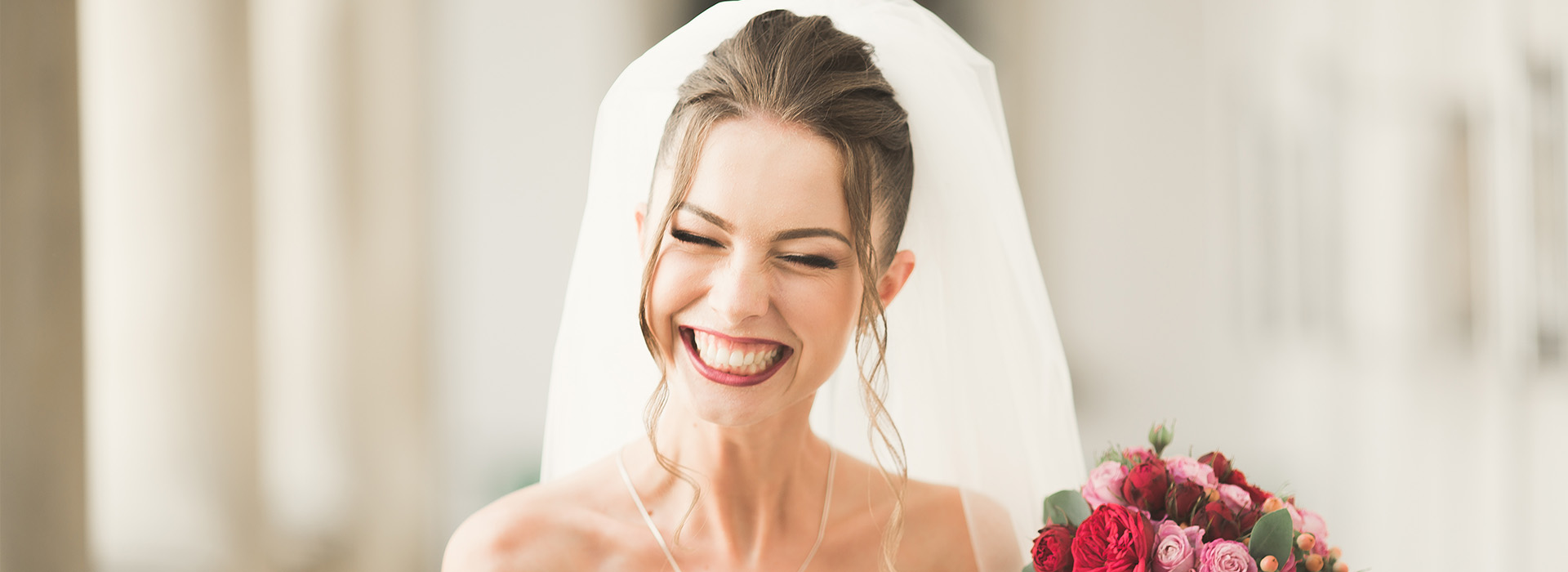 A bride in a white wedding dress, smiling and looking to the side, with her bouquet visible.