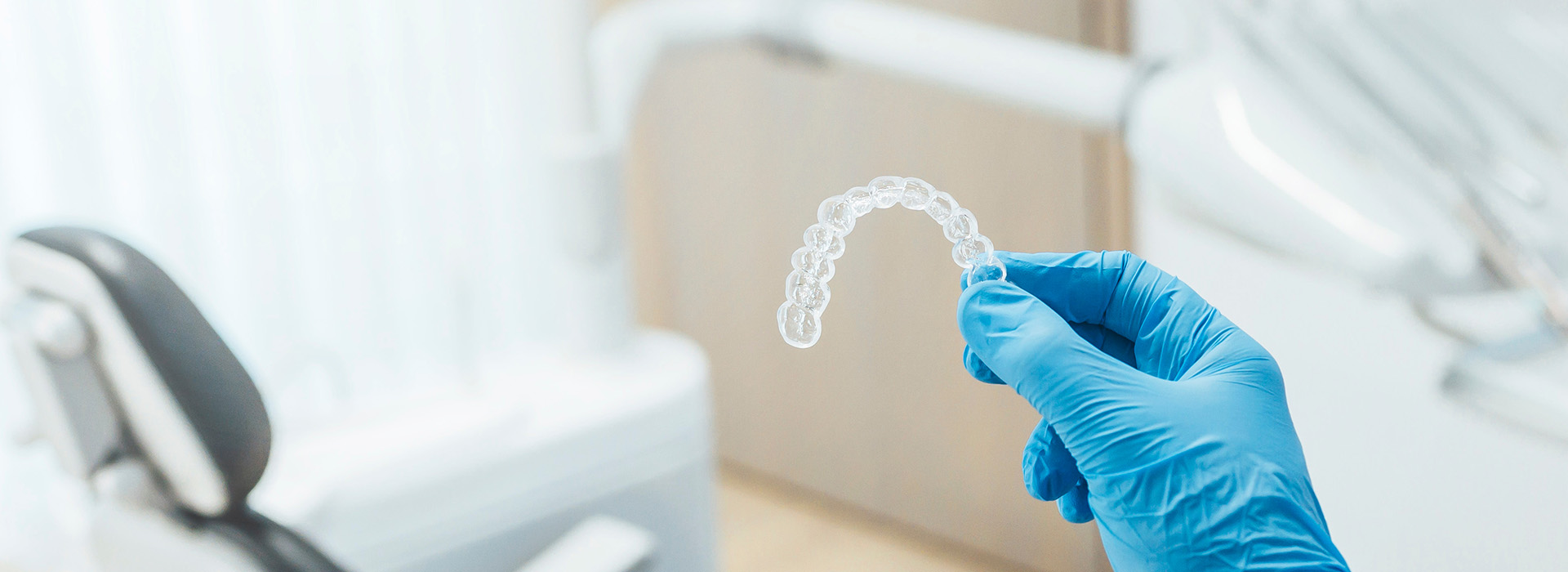 The image shows a pair of hands wearing blue gloves holding a transparent, clear dental impression material.