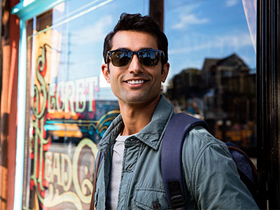 A man wearing sunglasses and a backpack, standing in front of a store window.