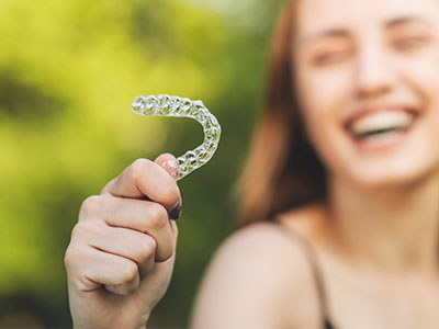 A smiling woman holding a clear plastic dental retainer with a toothpaste-like texture.