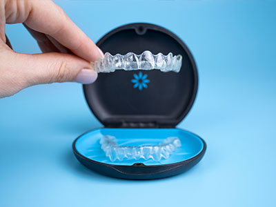 The image shows a person s hand holding an open case containing a set of clear aligners, which are part of an orthodontic treatment system like Invisalign.