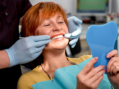 A woman in a dental chair, receiving a teeth cleaning, with a dental hygienist performing the procedure.