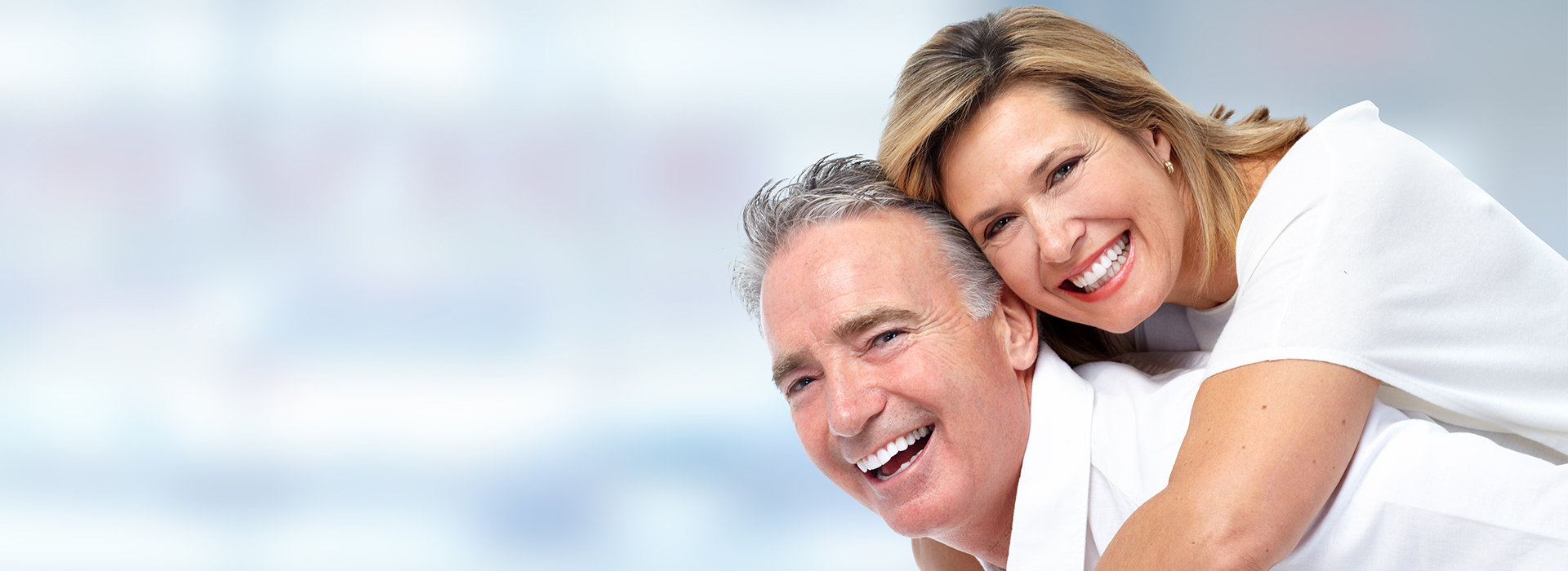 An elderly couple smiling and embracing each other, with the man wearing a white shirt and the woman in a light-colored top.