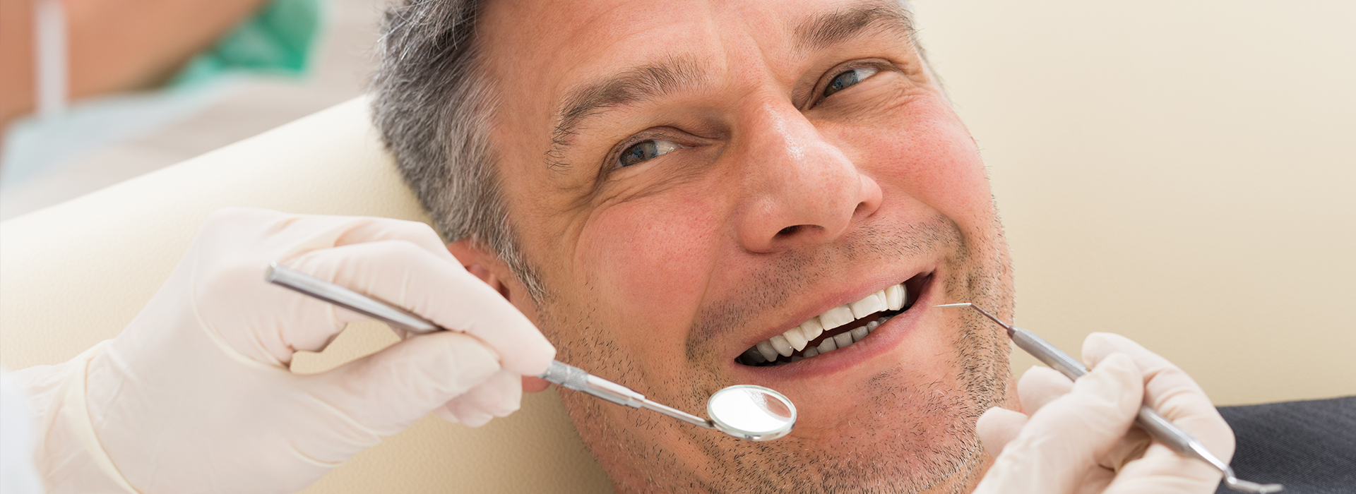 Dentist in a chair with his mouth open, smiling while receiving dental care.