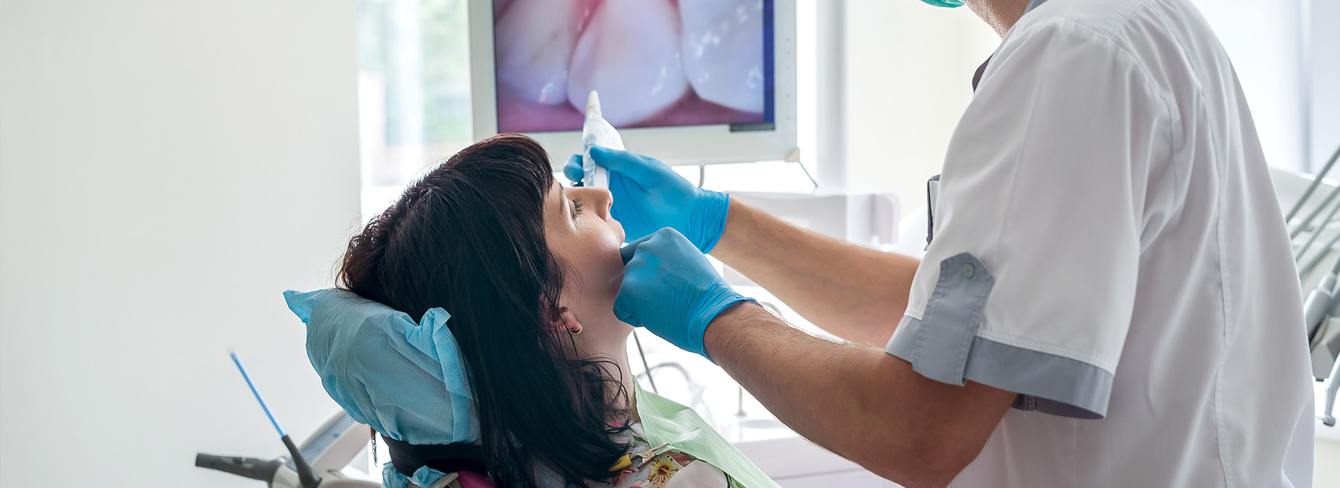 The image shows a dental hygienist cleaning a patient s teeth in an office setting.