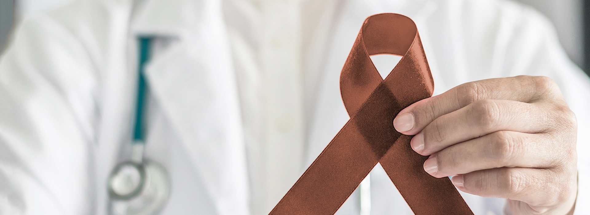 The image features a healthcare professional holding up a red ribbon with the word  cancer  written on it.