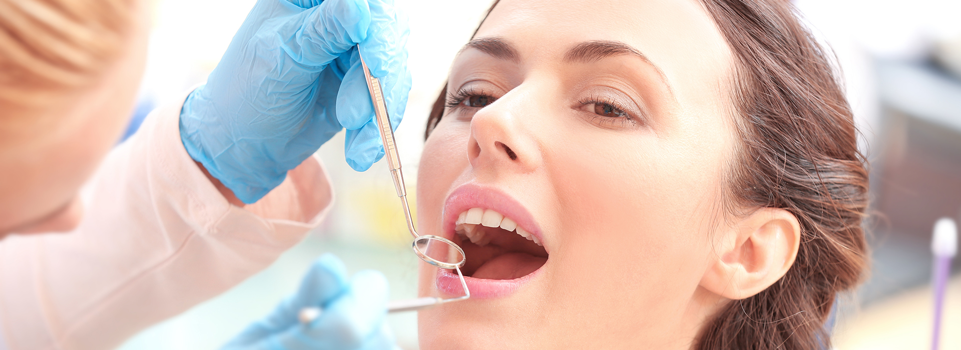 A dental hygienist is performing a teeth cleaning procedure on a patient, who is seated in the dentist s chair.