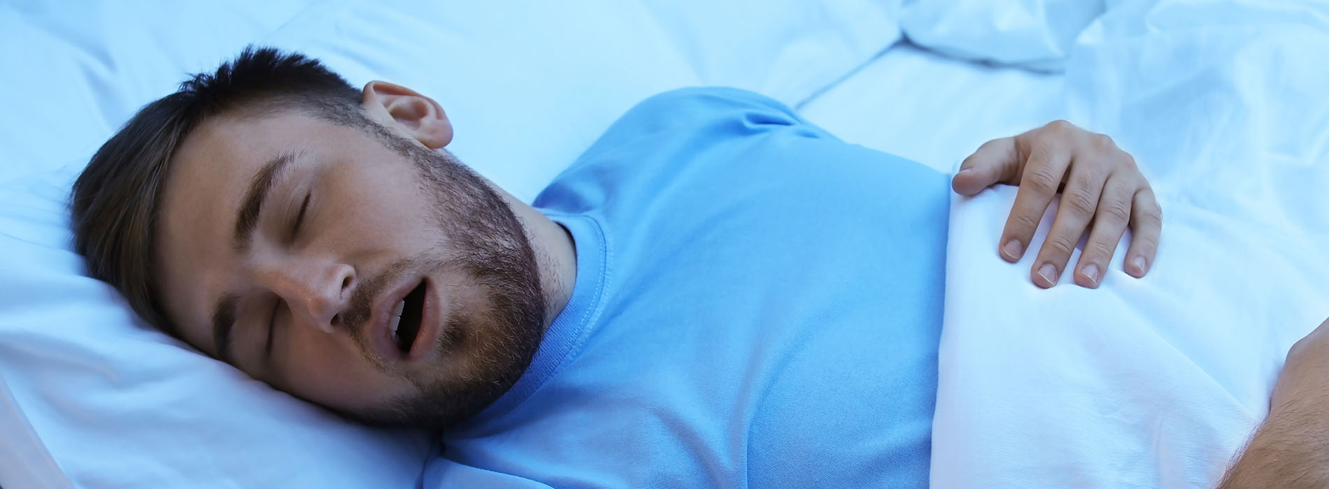 A man sleeping in a bed with his mouth open.