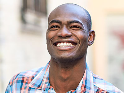 The image is a portrait of a smiling man with short hair, wearing a blue and white plaid shirt.