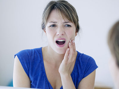 A woman in a blue top with her mouth open, expressing surprise or concern, while holding her hand to her face.