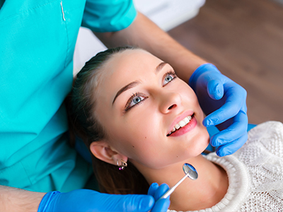 A female patient receiving dental care from a professional, with a smiling expression and blue gloves visible.