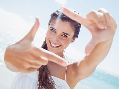 A woman taking a selfie with her hand held up in front of her face, against a clear sky background.