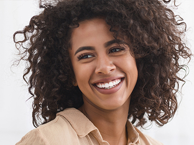 Smiling woman with curly hair and a bright smile, wearing a light-colored top, against a white background.